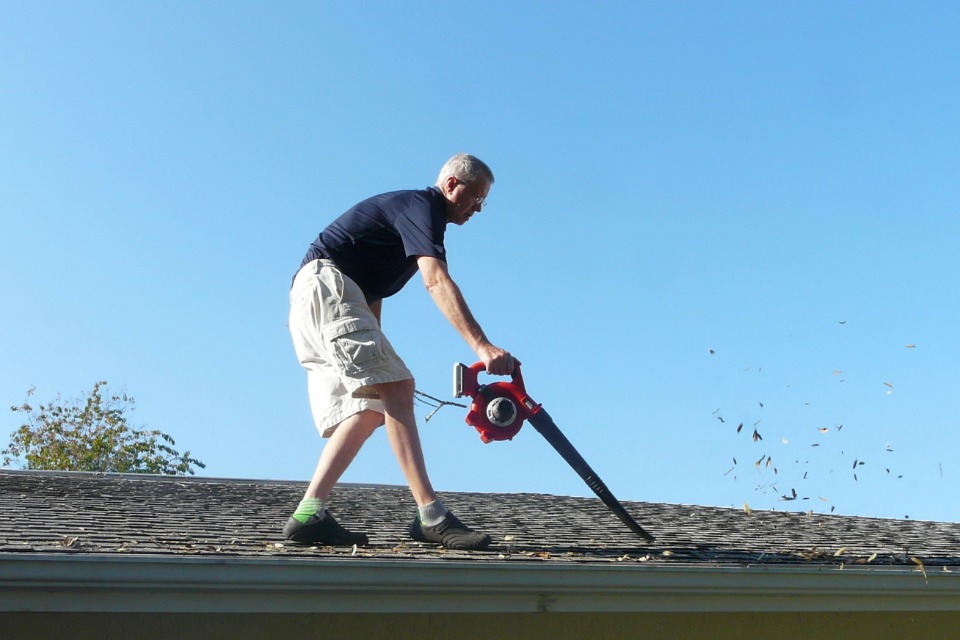 Man on roof using a leaf blower to clean his rain gutter showing one of the three best ways to clean gutters